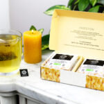 Coffret digestion de 12 infusettes ouvert sur une table en marbre avec une tasse qui infuse à coté